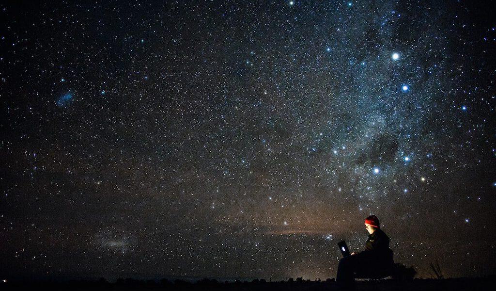 a remote digital worker with laptop outdoors at night under a starry sky