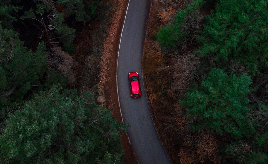 overhead photo of a red SUV driving on a windy country road at dusk