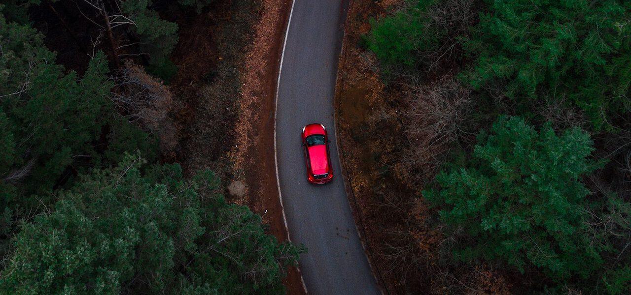overhead photo of a red SUV driving on a windy country road at dusk