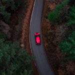 overhead photo of a red SUV driving on a windy country road at dusk