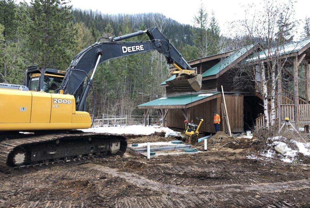 excavator and crew placing septic tanks next to a barn-loft
