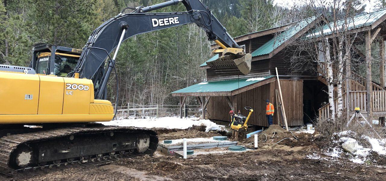 excavator and crew placing septic tanks next to a barn-loft