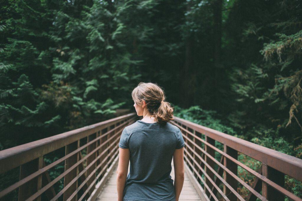 woman facing a pedestrian bridge into a forest
