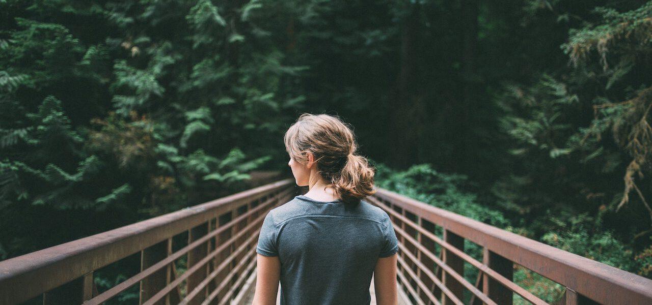 woman facing a pedestrian bridge into a forest